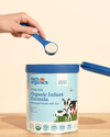 Nara Organics Organic Whole Milk Infant Formula can with a hand holding a scoop of powder.